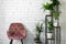 minimalism interior with pink chair and stand with green houseplants on white brick wall background