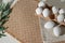 Minimalist aestethic Easter background with white eggs in eco package and green plant on a sand color jute rug, spring flat lay,