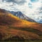 Minimalist autumn landscape with  sunlit orange mountainside on background of mountains silhouettes on horizon. Minimal mountain