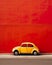 Minimalist background featuring a small car parked on a vibrant city street against a colorful wall.