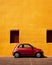 Minimalist background featuring a small car parked on a vibrant city street against a colorful wall.