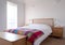 Minimalist bedroom interior with wooden bedroom furniture, white painted walls, white bedding and colourful blanket.