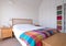 Minimalist bedroom interior with wooden bedroom furniture, white painted walls, white bedding and colourful blanket.