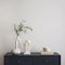 Minimalist composition of elegant and outstanding space with copy space, navy commode, green leaves in vase books, sculpture and