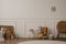 Minimalist composition of kids room interior with velvet orange armchair, braided baskets, round rug, white stool, beige wall with