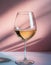 Minimalist glass of white wine on a pink background.