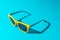 Minimalist photo of stylish yellow sunglasses with harsh shadow as summer concept.