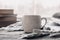 Minimalist style. Coffee, cozy grey sweater and books on vintage windowsill against snow landscape from outside. Soft