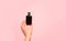 Minimalistic flat lay photo of a woman`s hand holding fragrant perfume in a stylish black glass bottle on a pastel pink backgroun