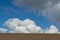 Minimalistic landscape with plowed soil and blue sky with big fluffy clouds