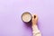 Minimalistic style woman hand holding a cup of coffee on Colored background. Flat lay, top view cappuccino cup. Empty