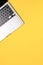 Minimalistic vertical flat lay photo on a yellow background with a modern silver grey laptop with a black keyboard