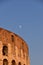 Minimalistic vertical shot of the Colosseum on the background of a warm blue sky with the moon