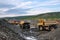 Mining trucks are queuing, in the background a wheel loader is loading mountain soil into the bodies of these trucks