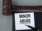 MINOR ABUSE - words on a white sheet with leather notebooks, a judge\\\'s hammer and a pen