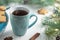 Mint cup of tea with heart, gingerbread next to branches of a Christmas tree with ight bulbs on white wooden background