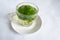 Mint tea leaves in hot water in a glass mug with a handle on a white saucer. The table has a white paper tablecloth