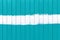 Mint, turquoise or aquamarine metal wall fence with vertical corrugated stripes and with a horizontal stripe of white paint