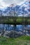 Mirror Image of Trees and Sky Along a Calm River.