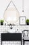 Mirror between plant and poster in white and black bathroom interior with chair. Real photo