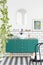 Mirror and poster above green cabinet in bathroom interior with black chair and plants. Real photo