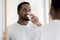 Mirror reflection satisfied African American man drinking mineral water