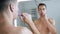 Mirror reflection of young bare man brushing his teeth with toothbrush and toothpaste in the morning doing hygiene