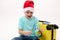 Mischievous teenage boy in Santa hat, sitting next to yellow suitcase, points to a travel destination on globe. Tourism
