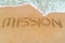 MISSION inscription written on sandy beach with wave approaching