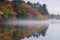 Mist hovers along a lake reflecting a New England autumn.