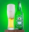 misted and slightly frosty bottle of heineken beer with a mug of poured beer with foam. green background.