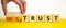 Mistrust or trust symbol. Businessman turns wooden cubes, changes words `mistrust` to `trust`. Beautiful yellow table, white