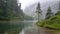 Misty alpine lake with green pine trees and mountain background