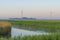 Misty canal in an agricultural field below a blue yellow sky in sunlight at a foggy sunrise in a spring morning