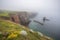 misty coastal cliff, with view of the ocean and boats in the distance