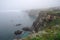 misty coastal cliff, with view of the ocean and boats in the distance