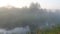 Misty dawn at the river, beautiful summer morning in wood with sun rays and a fog from the river