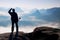 Misty day in rocky mountains. Silhouette of tourist with poles in hand. Hiker stand on rocky view point above misty valley.