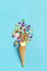 Mix colorful chocolate sweets spilled out of ice cream waffle cone on blue background