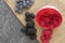 Mix of Red raspberries falling from a ceramic plate and a bunch of blackberries and blueberries in a rattan and black background.