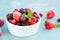 Mix of summer frozen berries in a white bowl on a blue concrete background. Copy space
