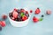 Mix of summer frozen berries in a white bowl on a blue concrete background. Copy space