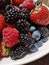 Mixed fruit berries on white plate. Closeup of forest fruits. Summer fruit