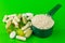 Mixed natural food supplement pills and protein powder in plastic spoon on green background.