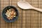 Mixed nuts in black bowl with wooden spoon over brown bamboo mat.