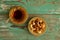 Mixed nuts on a yellow metal saucer and a glass cup of Turkish tea on a turquoise wooden background.