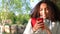 Mixed race African American girl teenager leaning against a tree using a cell phone camera for social media