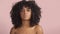 Mixed race black woman with curly hair covered by crystal makeup on pink background in studio