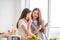 Mixed race girl younger and older sister talk and smile while play and using smartphone inside of the kitchen in the morning while