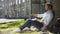 Mixed-race guy sitting under tree, waving and smiling at somebody, friendly